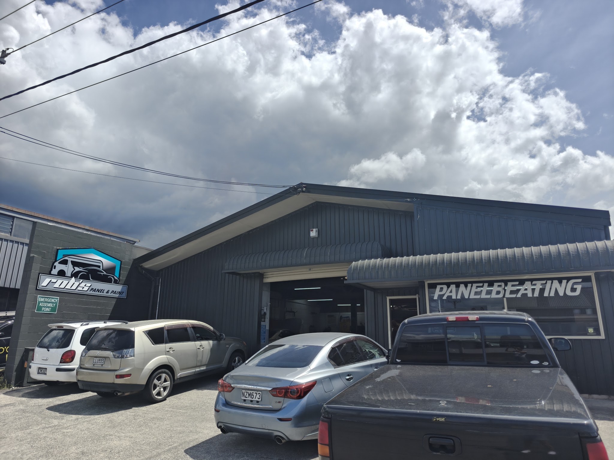 Rob's Panel & Paint shopfront on Riri Street, Mangakakahi, with the roller door open and customer vehicles parked outside